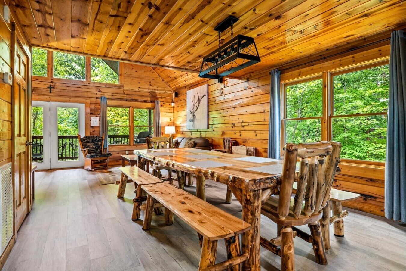 A rustic cabin interior with a large wooden dining table, benches, and a cozy seating area.