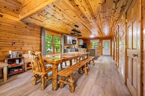 Ein Holzblockhaus-Interieur mit einem Holzesstisch, Stühlen, einer Küchenzeile und einem großen Fenster.