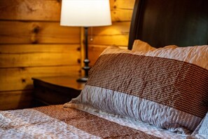A bed with a patterned blanket and pillows, a wooden wall, and a nightstand with a lamp. - 5 Min to Pigeon Forge! 5BR*Hot Tub*Fire Pit*Quiet (Pigeon Forge)