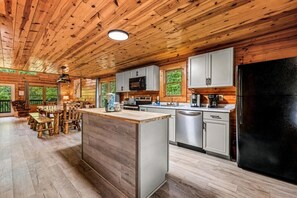 Ein Ferienhausinnenraum mit Holzbalkendecke, einer zentralen Kochinsel mit Spüle, Mikrowelle, Herd und Kühlschrank.