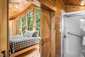 Ein Schlafzimmer einer Holzhütte mit Bett, Fenster und Dusche.