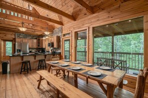 A wooden cabin interior with a dining area, kitchen, and large windows overlooking a forest. - Stunning MTN Views! Hot Tub*Pool Table*Privacy! (Gatlinburg)