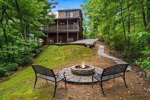 A two-story cabin with a stone exterior, a deck, and a fire pit with two chairs. - Stunning MTN Views! Hot Tub*Pool Table*Privacy! (Gatlinburg)