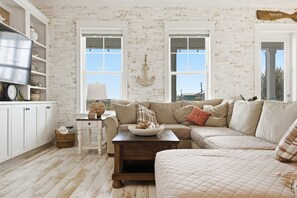 A living room with a sectional sofa, a wooden coffee table, and a television on a white cabinet. - Beach Days • S’mores • Sound Views • Just Beachy (Navarre Beach)