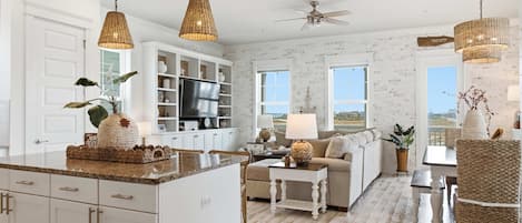 A spacious kitchen with white cabinetry, a central island, and a dining area with wicker chairs.