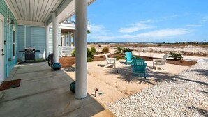 Eine überdachte Veranda mit Sitzgelegenheiten im Freien, einem Grill und Blick auf den Strand.