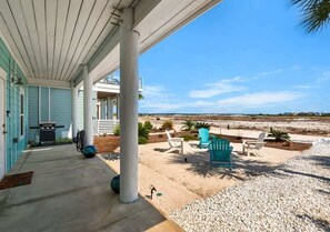 Eine überdachte Veranda mit Sitzgelegenheiten im Freien, einem Grill und Blick auf den Strand.