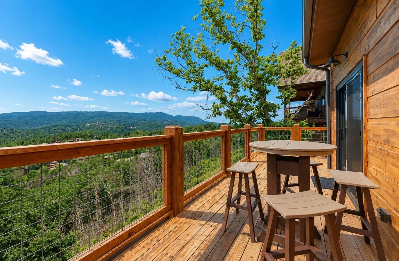 Eine Holzdielen-Terrasse mit Tisch und Stühlen mit Blick auf eine gebirgige Landschaft.