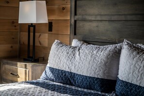 Een bed met een gewatteerd hoofdbord, een nachtkastje met een lamp, en een houten wand.