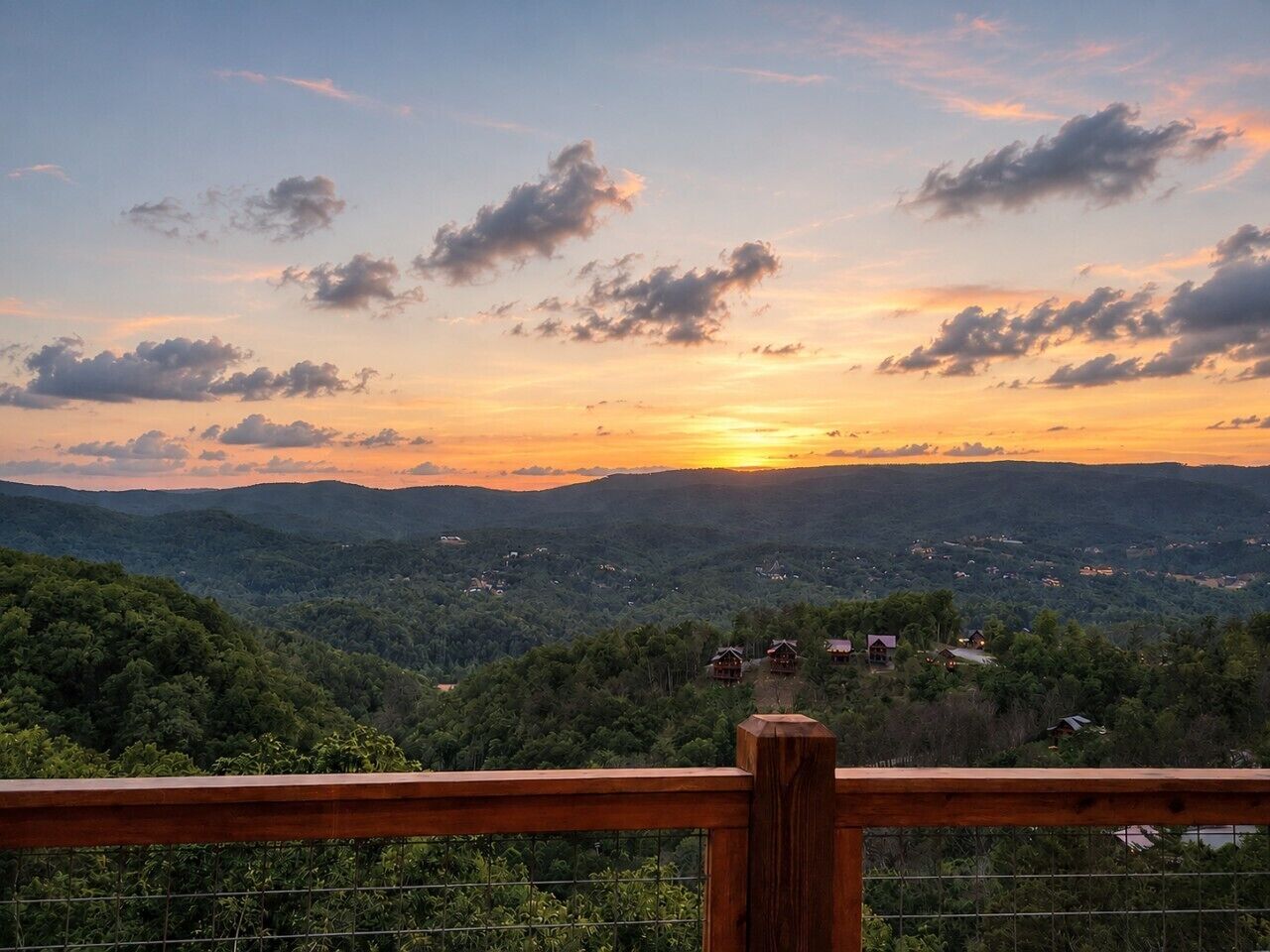 A scenic view from a wooden balcony overlooking a valley with scattered houses and dense forest.
