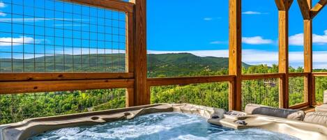 A hot tub with a wooden deck and a view of green hills.