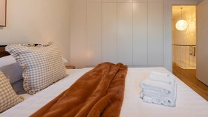 Ett hotellrum med en säng, rutiga kuddar, en brun filt och prydligt hopvikta handdukar.