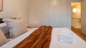 Ein Hotelzimmer mit einem Bett, Karokissen, einer braunen Decke und ordentlich gefalteten Handtüchern.