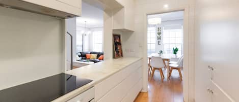 Une cuisine moderne avec des meubles blancs, une plaque de cuisson à induction noire et un coin repas comprenant une table et des chaises blanches.