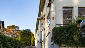 Ein mehrstöckiges Gebäude mit weißer Fassade, Klimaanlagen und einem Balkon mit Metallgeländer.