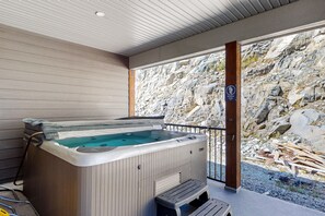 A hot tub with a wooden exterior, a bench, and a view of rocky terrain through a glass door. - SS Monashee by Okanagan Premier (Beaverdell)