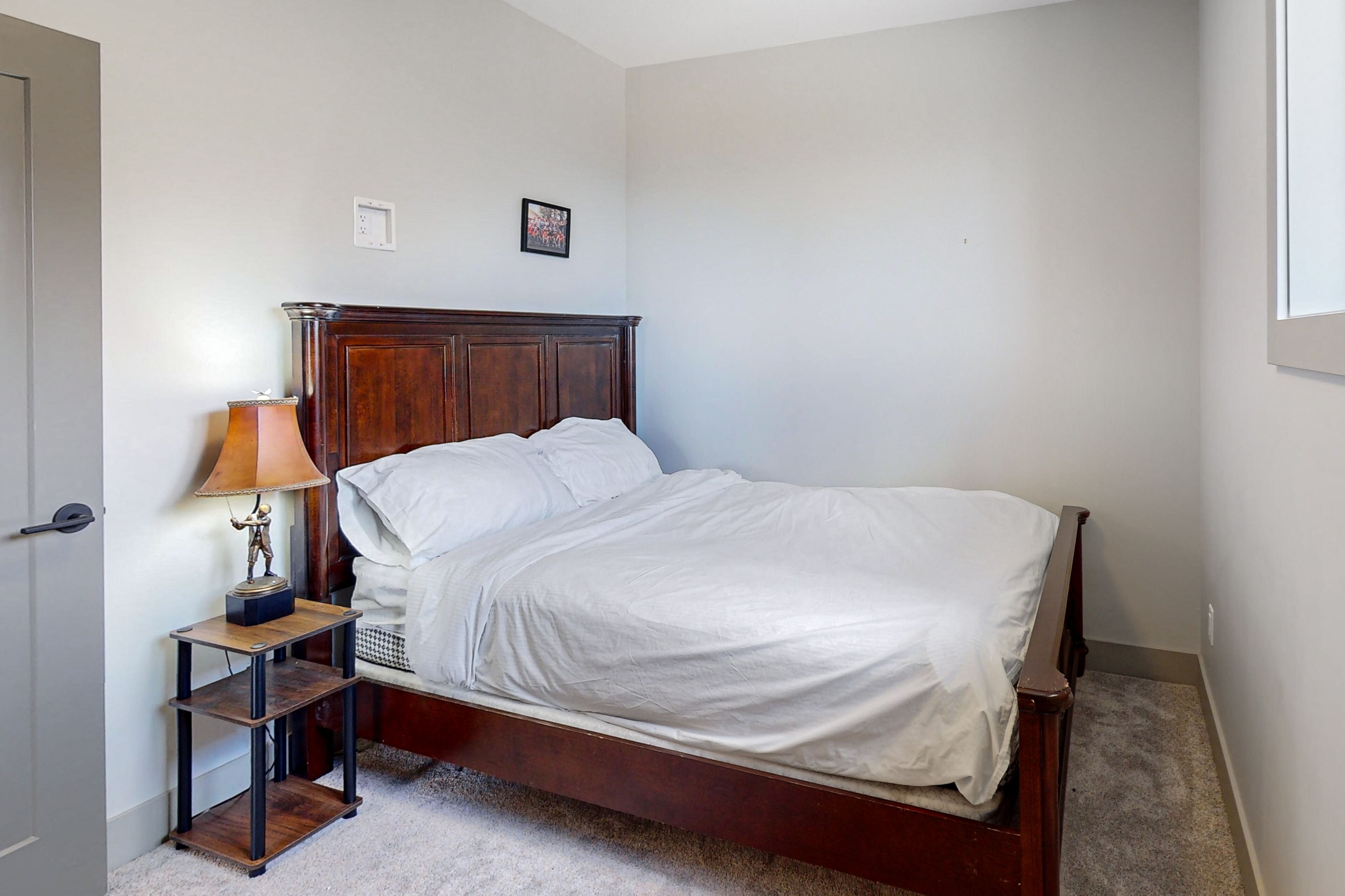 A bedroom with a wooden bed, a nightstand with a lamp, and a small shelf.