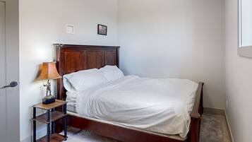 A bedroom with a wooden bed, a nightstand with a lamp, and a small shelf.