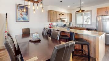A modern kitchen with wooden cabinets, a stainless steel refrigerator, and a dining area with a wooden table and leather chairs.