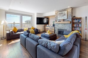 A modern living room with a stone fireplace, a large flat-screen TV, and a bookshelf. - SS Monashee by Okanagan Premier (Beaverdell)