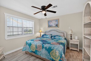 A bedroom with a bed, a ceiling fan, a window with blinds, a painting on the wall, and a nightstand with a lamp. - BEACHFRONT! FIRST ROW! Stunning ocean views from two levels of decks. (Surfside Beach)