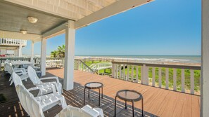 A covered outdoor area with a view of the beach, featuring a wooden deck, white plastic chairs, and wicker tables. - BEACHFRONT! FIRST ROW! Stunning ocean views from two levels of decks. (Surfside Beach)