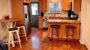 Una cucina con mobili in legno, un frigorifero in acciaio inox, una lavastoviglie e un bancone con sgabelli.