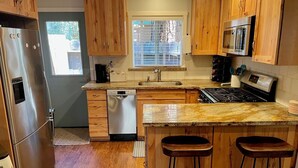 Una cucina con mobili in legno, un frigorifero in acciaio inox, una lavastoviglie, un piano cottura e una finestra con persiane.