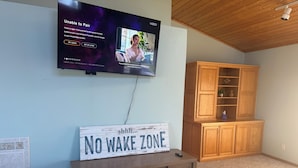 Uma sala de estar com televisão na parede, um armário de madeira e um aviso sobre uma mesa de console que diz 'NO WAKE ZONE'.