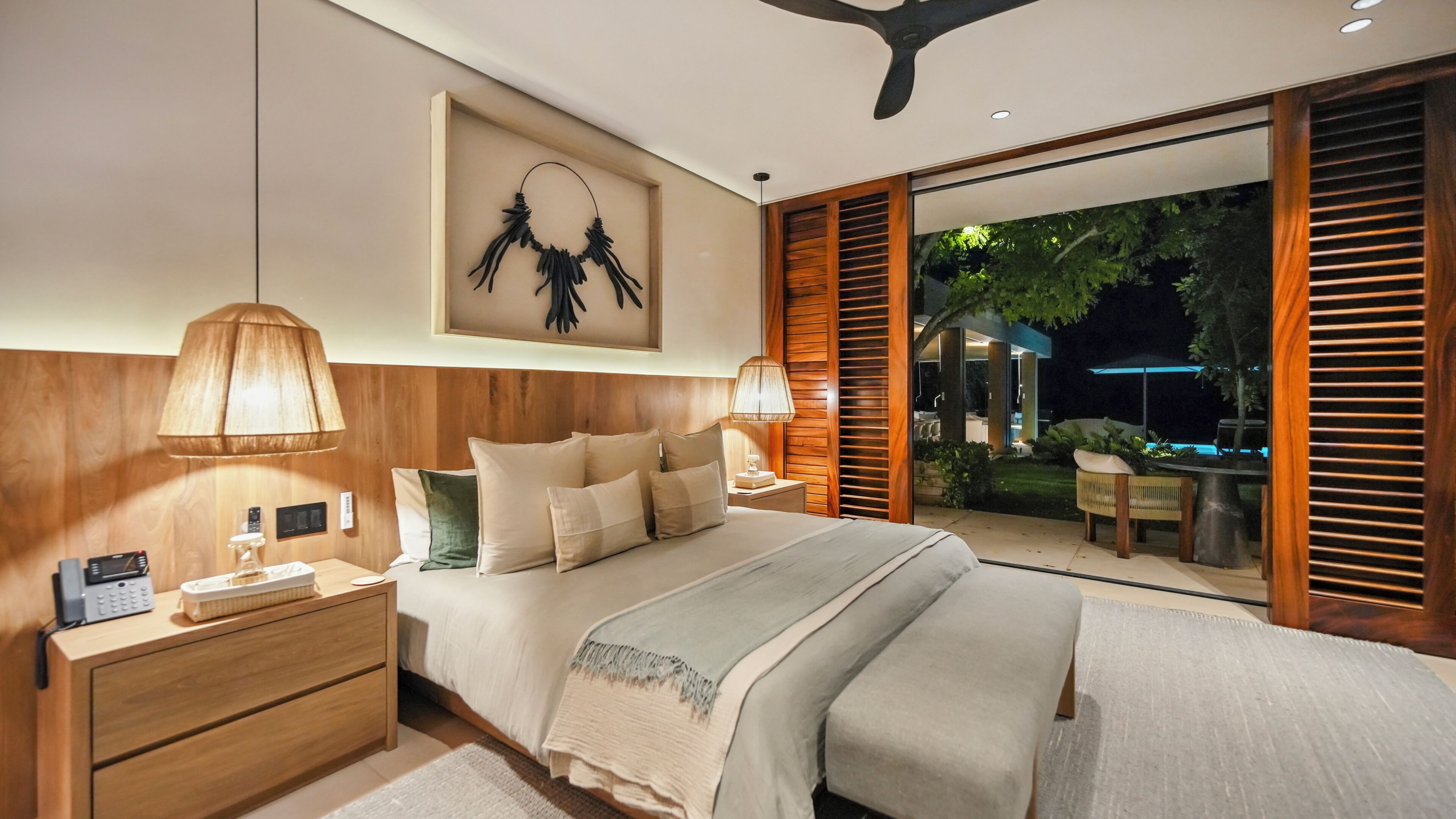 Ein modernes Schlafzimmer mit einem großen Bett, Nachttischen, einem Wandbild und Blick auf einen Garten.