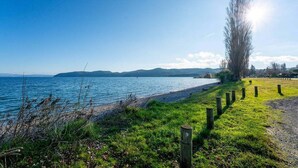A coastal landscape with a grassy area, wooden posts, and a clear view of the sea. - Tui Shack (Kinloch)