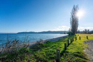 A coastal landscape with a grassy area, wooden posts, and a clear view of the sea. - Tui Shack (Kinloch)