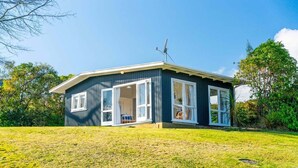 A single-story house with a large open porch, a satellite dish, and a grassy yard. - Tui Shack (Kinloch)
