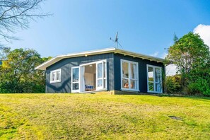 A single-story house with a large open porch, a satellite dish, and a grassy yard. - Tui Shack (Kinloch)