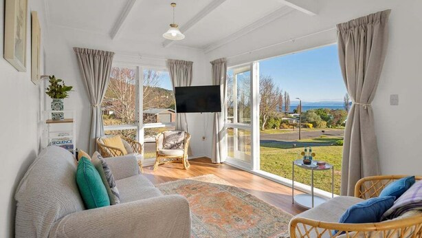A spacious living room with a large window, a flat-screen TV, and a comfortable seating area. - Tui Shack (Kinloch)