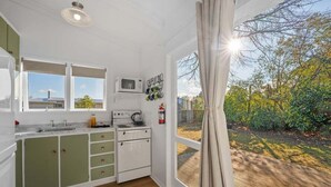A kitchen with a microwave, stove, and cabinets, a window with a view of greenery, and a curtain. - Tui Shack (Kinloch)