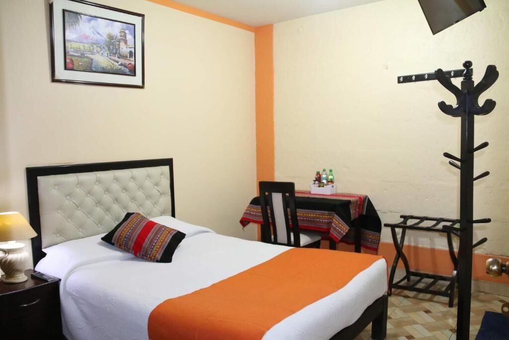 Habitación de hotel con cama, una mesa y sillas, perchero y un cuadro en la pared.