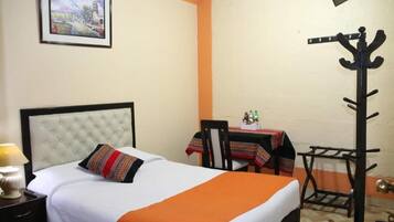 Habitación de hotel con cama, una mesa y sillas, perchero y un cuadro en la pared.