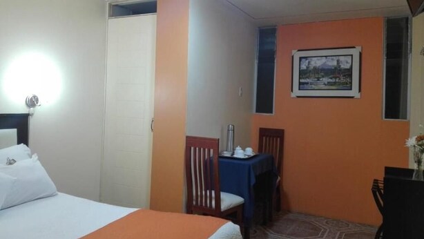 A hotel room with a bed, a desk, a chair, a small table, and a framed picture on the wall. - Qori Arequipa (Arequipa)