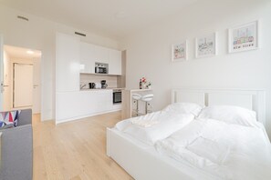 A modern hotel room with a white bed, a kitchenette, and a dining area. - The Elegant White Suite in SmichovCity Residence (Prague)