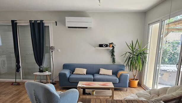 A modern living room with a blue sofa, wooden flooring, and a large window providing natural light. - Well-equipped house with air conditioning and a spa (Saint-Avit)