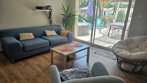 A living room with a sofa, a coffee table, a chair, and a view through a glass door to an outdoor patio. - Well-equipped house with air conditioning and a spa (Saint-Avit)