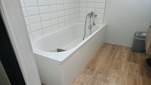 A bathroom with a white bathtub, wooden flooring, and a tiled wall. - Well-equipped house with air conditioning and a spa (Saint-Avit)
