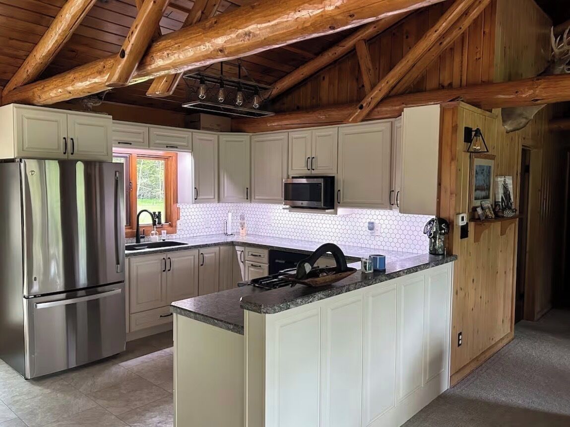 A kitchen with white cabinets, a stainless steel refrigerator, a microwave, and a wooden ceiling.