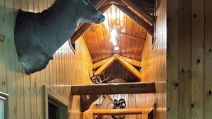 En hall med träpanel på väggarna, en taklampa, ett upphängt rådjurshuvud och ett inramat fotografi på väggen.