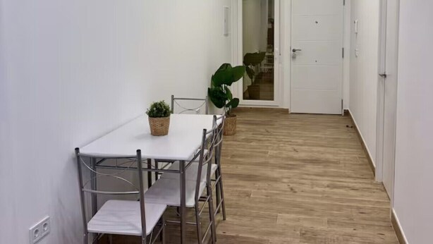 Un couloir étroit qui mène à un coin repas comprenant une table et des chaises, une plante en pot et une porte donnant sur une autre pièce.