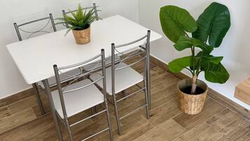 Een eettafel met metalen stoelen, een potplant en een grote, bladrijke plant ernaast.