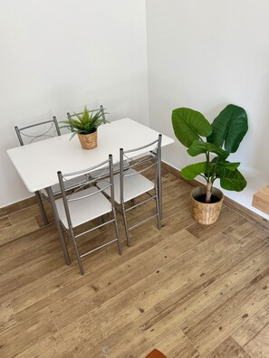 Een eettafel met metalen stoelen, een potplant en een grote, bladrijke plant ernaast.