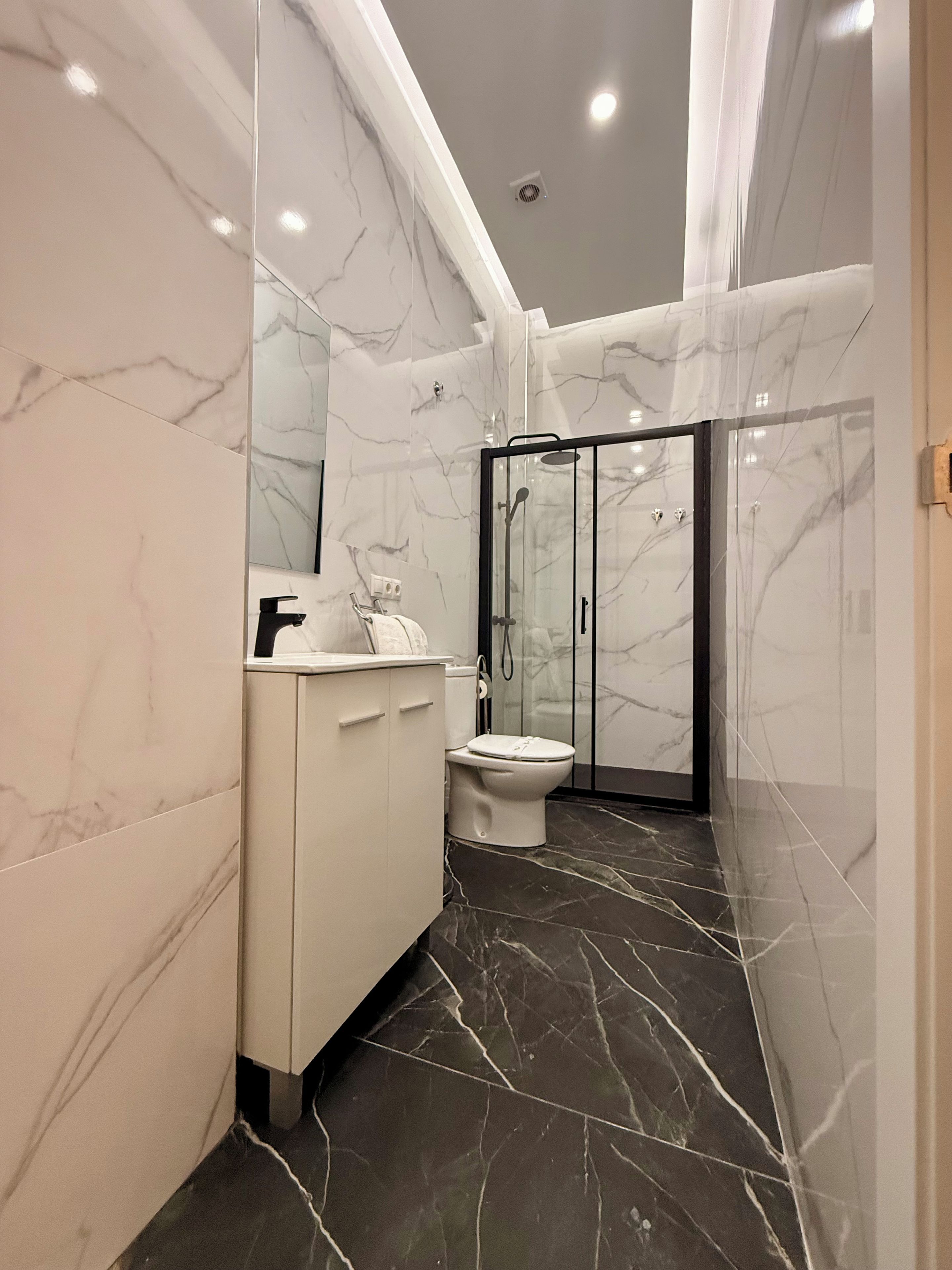 A modern bathroom with marble walls, a white vanity, a toilet, and a glass-enclosed shower area.