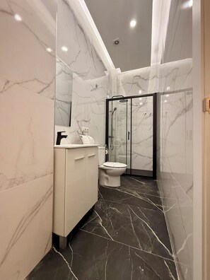 Een moderne badkamer met marmeren wanden, een witte wastafel, een toilet en een douchecabine met glazen wanden.